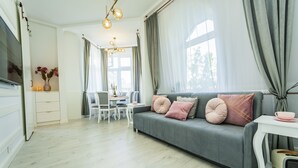 A modern living room with a grey sofa, white dining table, and a TV on the left. - Baltic Apartments-Willa Carmen 14 (Swinoujscie)