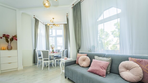 A modern living room with a grey sofa, white chairs, a dining table, and a chandelier. - Baltic Apartments-Willa Carmen 14 (Swinoujscie)