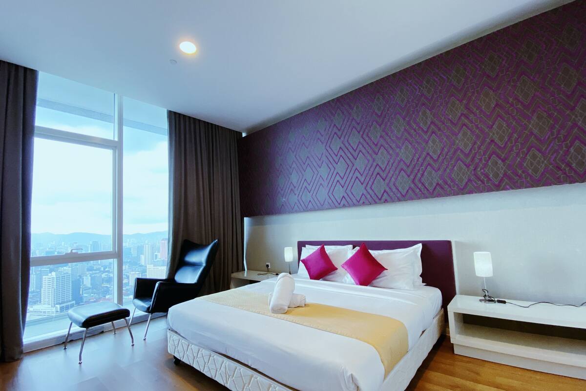 A hotel room with a large window, a bed with white bedding, a nightstand, and a chair.