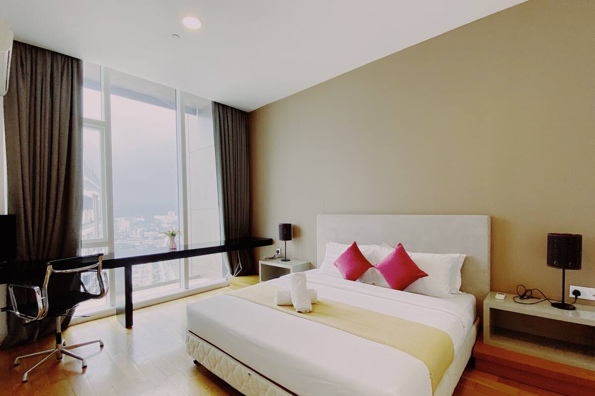 A hotel room with a large bed, a desk, a chair, a nightstand, and a view of the city.
