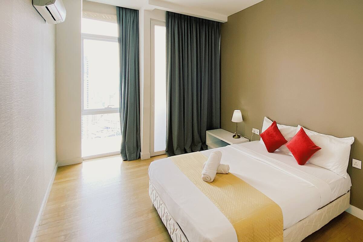A hotel room with a bed, a nightstand, a lamp, and a window with curtains.