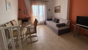 A living room with a sofa, TV, dining table, chairs, and a window with curtains. - Corfu Island Apartment 91 (Corfu)