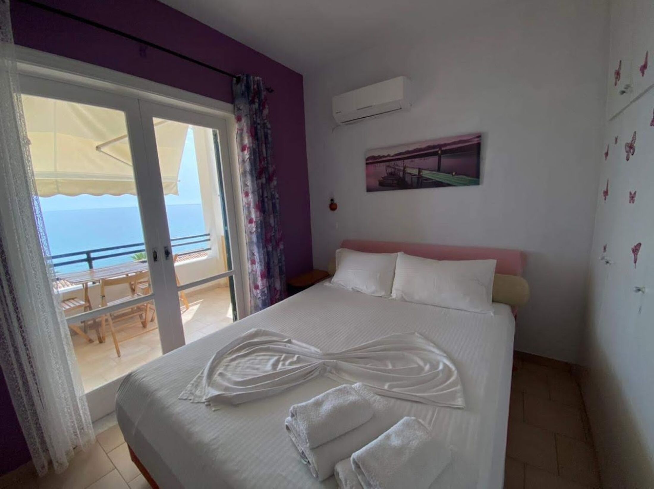 Une chambre d’hôtel avec un lit, un tableau et une vue sur la mer, visible à travers une porte coulissante.