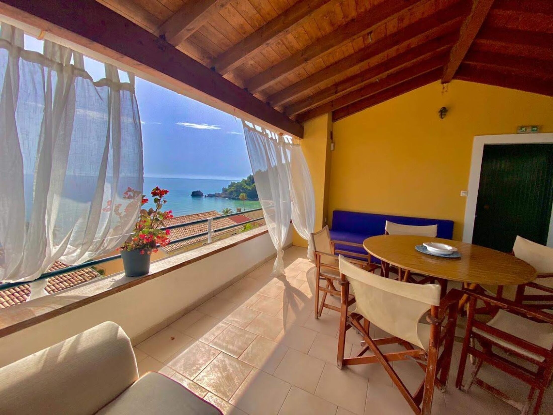 A balcony with a view of the sea, a table with chairs, and a sofa.