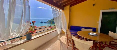A balcony with a view of the sea, a table with chairs, and a sofa.