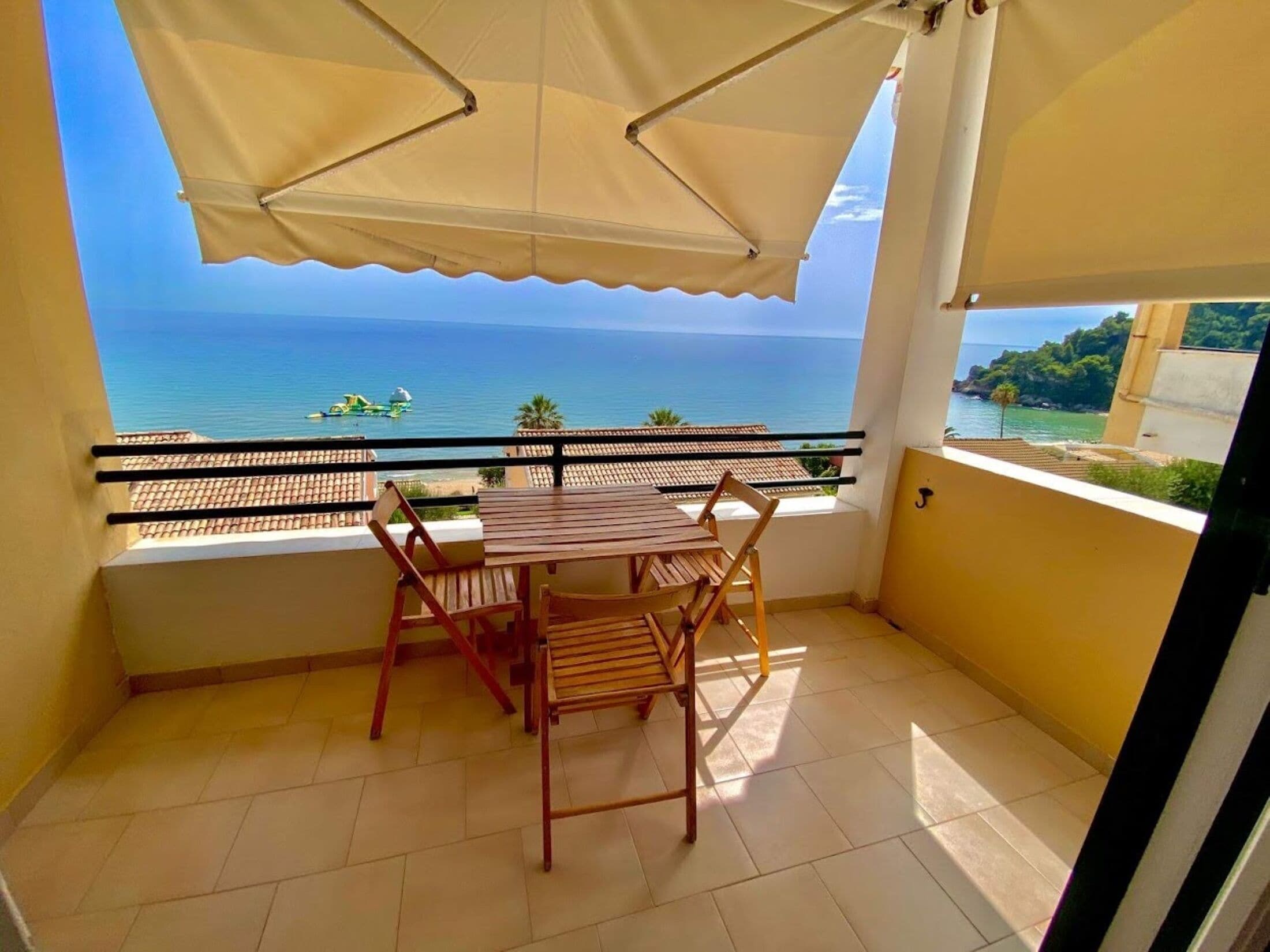 A balcony with a table and chairs, overlooking a coastal view with the sea and boats.