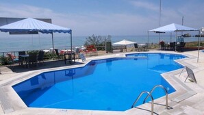 A swimming pool with a clear view of the sea, surrounded by lounge chairs and umbrellas. - Corfu Island Apartment 91 (Corfu)