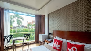 A hotel room with a large bed, a desk, and a chair. There is a window with curtains, a TV, and a patterned wall. - Ban-aw Candon (Candon)