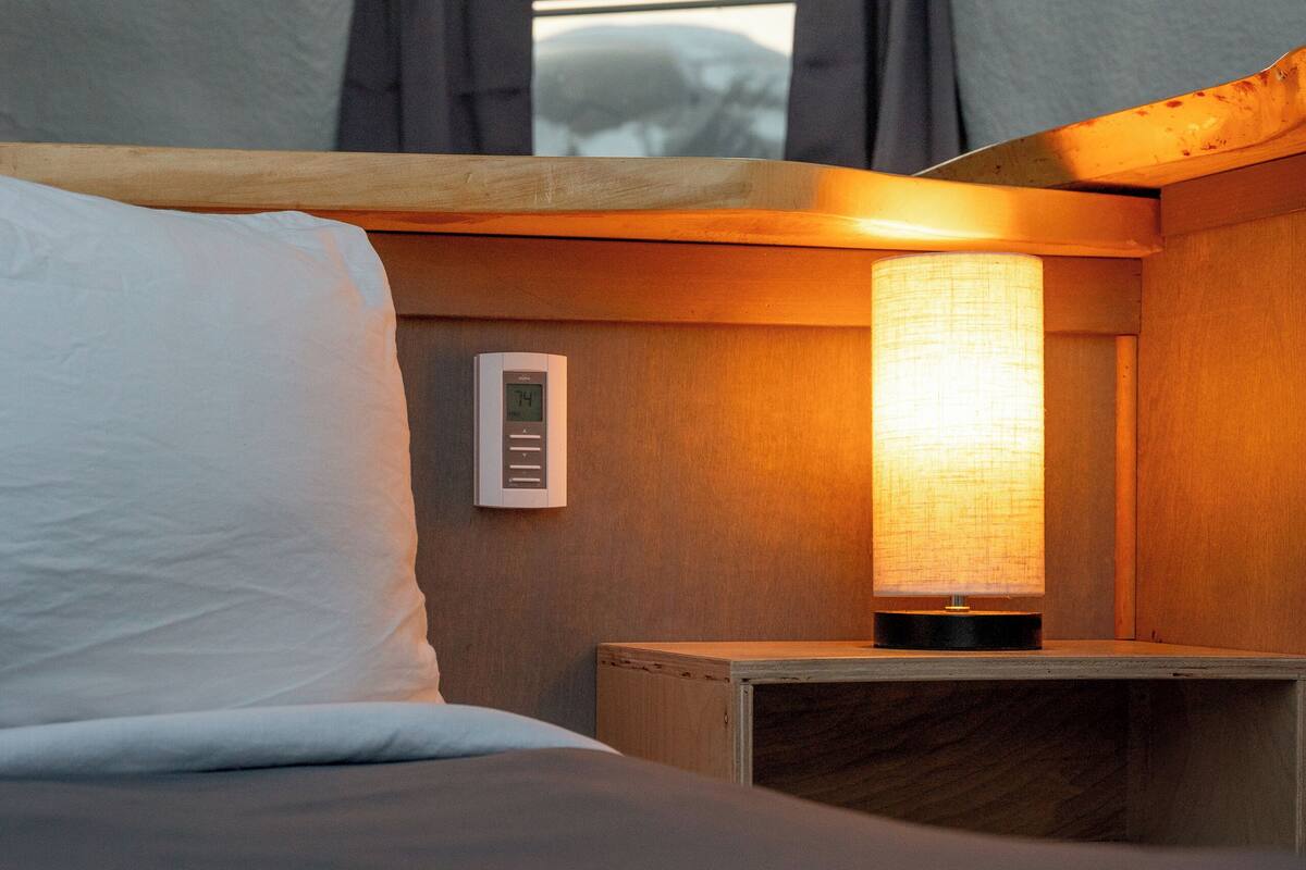 Un dormitorio con cama, mesita de noche, lámpara y ventana con cortinas.