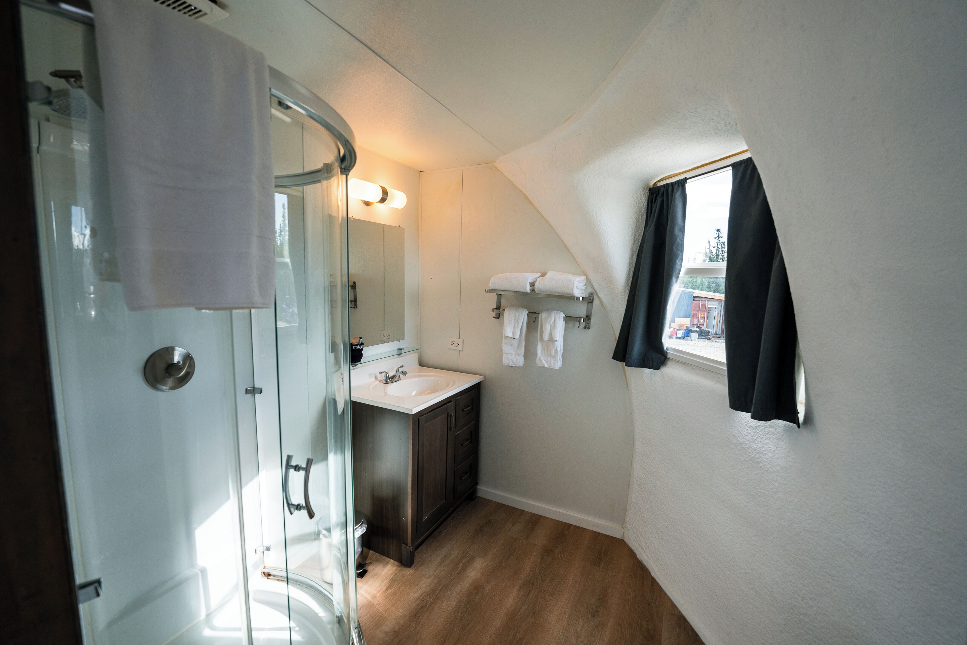 Ett modernt badrum med en duschkabin i glas, ett handfat och ett litet fönster med gardiner.