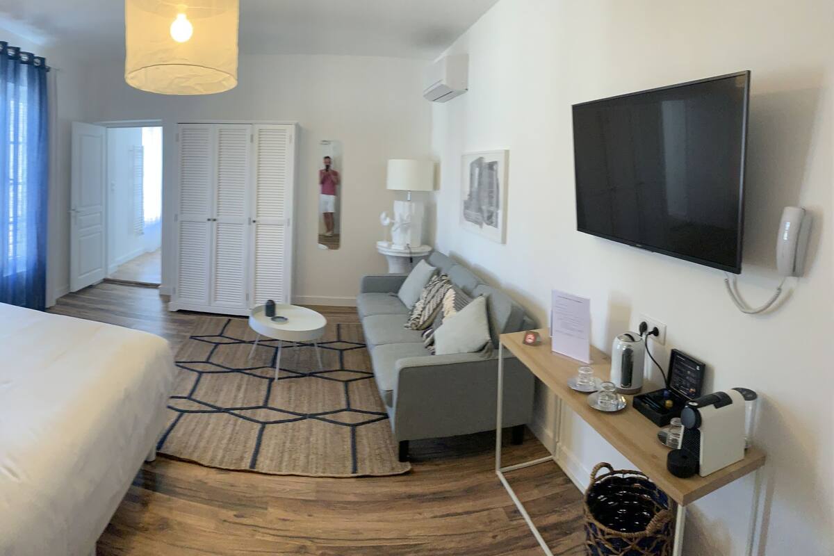Habitación de hotel con cama, mesita de noche, lámpara, televisor y un pequeño rincón de descanso con sofá y mesa.
