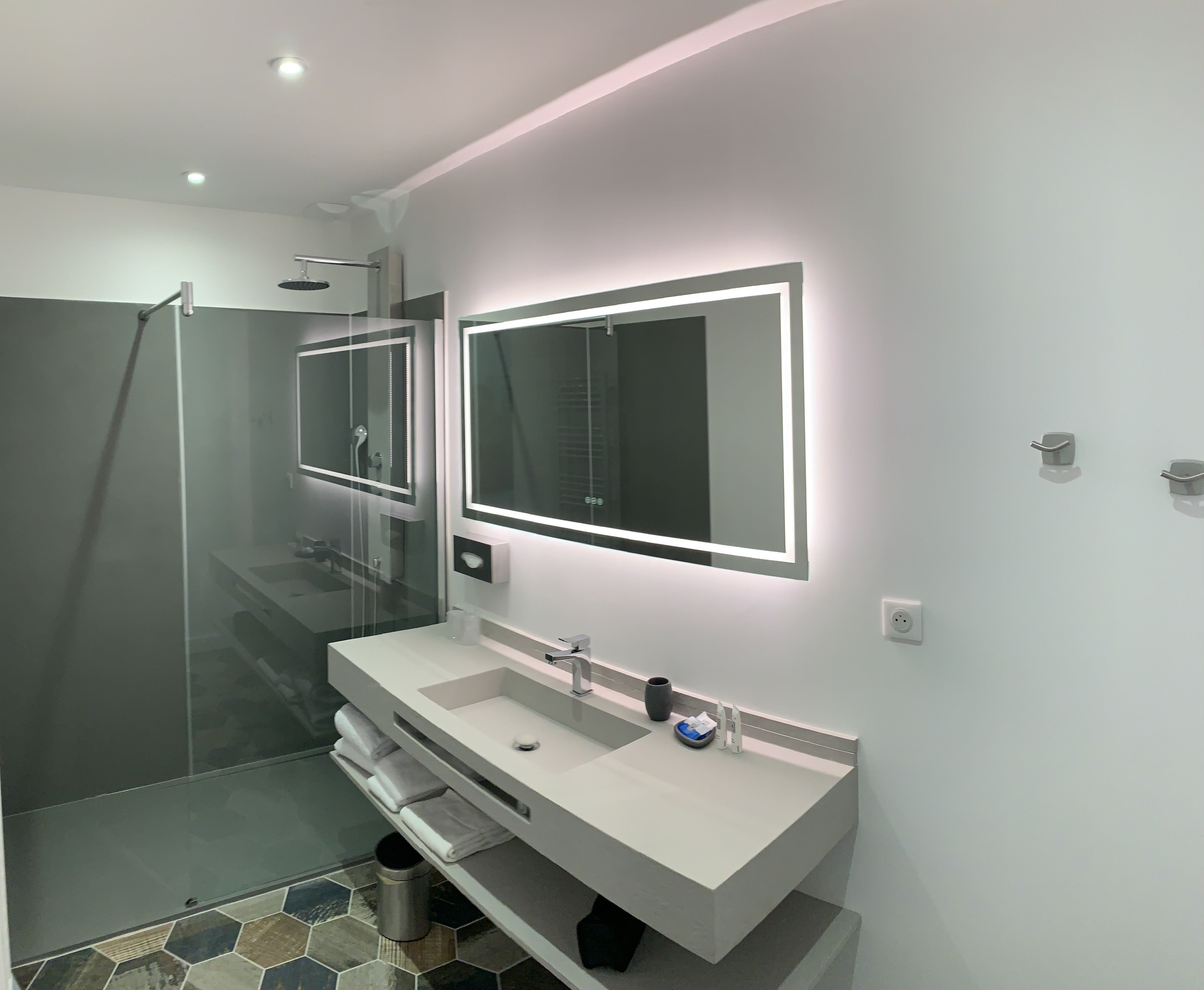 A modern bathroom with a glass shower enclosure, a large mirror, and a white vanity with a sink.
