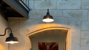 Un couloir avec un mur en pierre, une grande peinture abstraite et deux lampes fixées au mur.