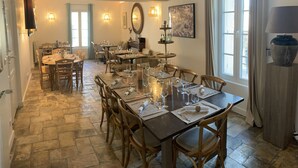Un espace repas avec plusieurs tables dressées pour le repas, un sol en pierre et des luminaires fixés au mur.