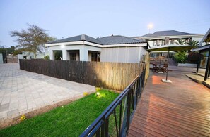 Ein modernes Haus mit gepflasterter Terrasse, einer Holzterrasse und einem umzäunten Garten.