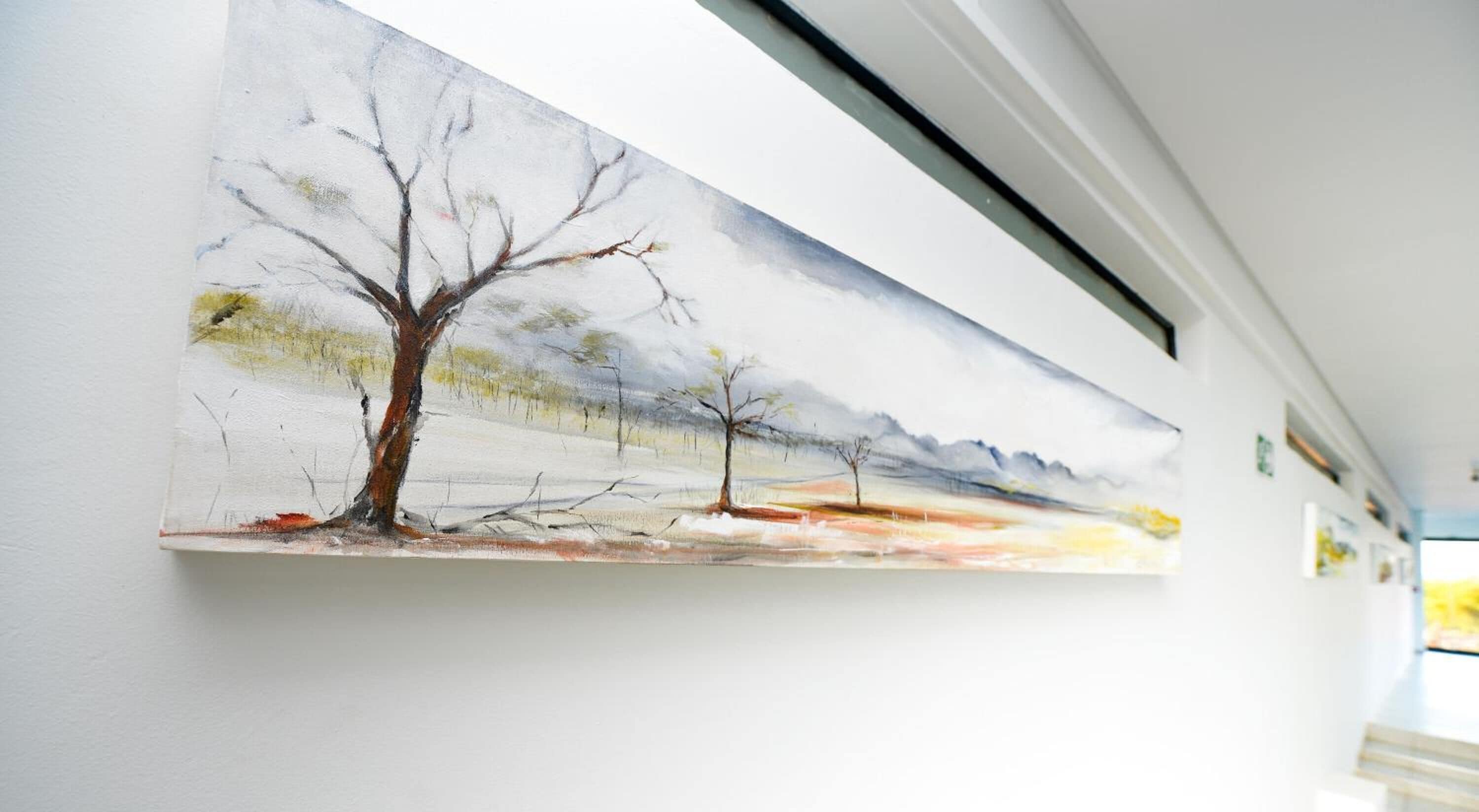 Een schilderij van een winterlandschap met kale bomen en een besneeuwde grond, hangend aan een muur.