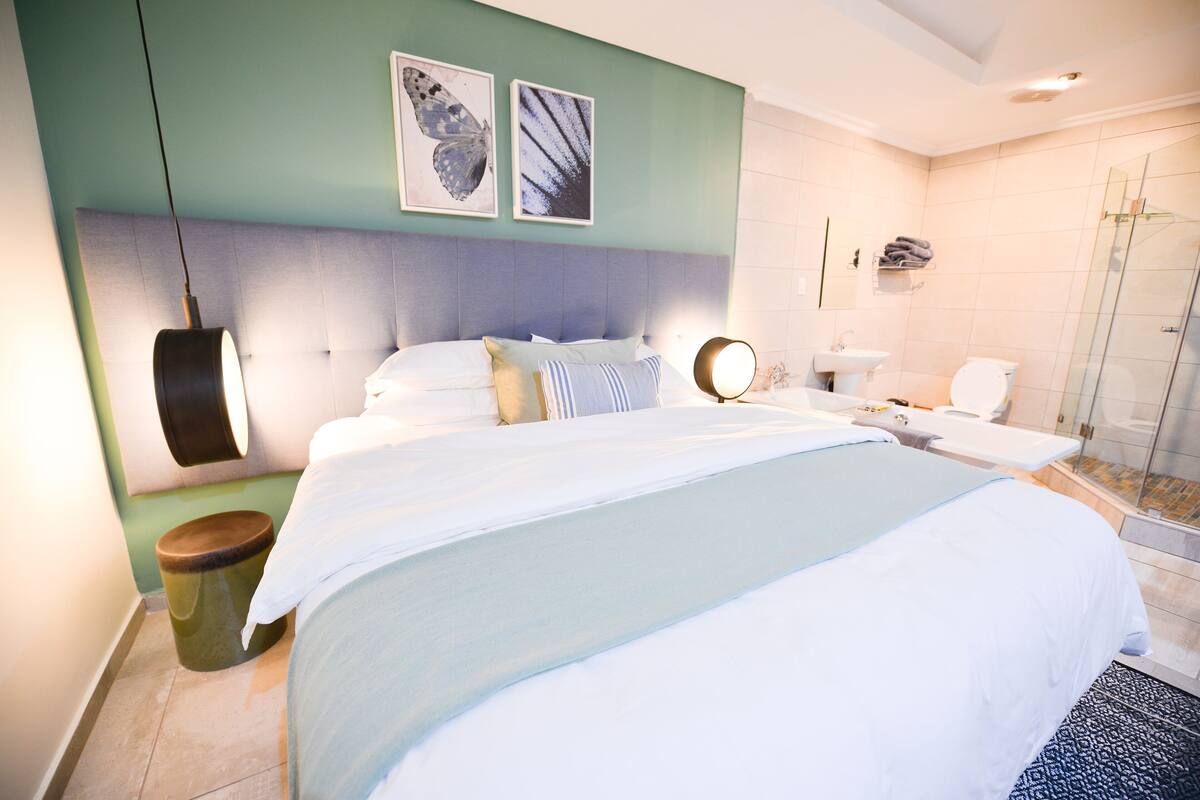 Ein modernes Schlafzimmer mit einem großen Bett, einem Nachttisch, einem Spiegel und einem Badezimmer mit Duschkabine.