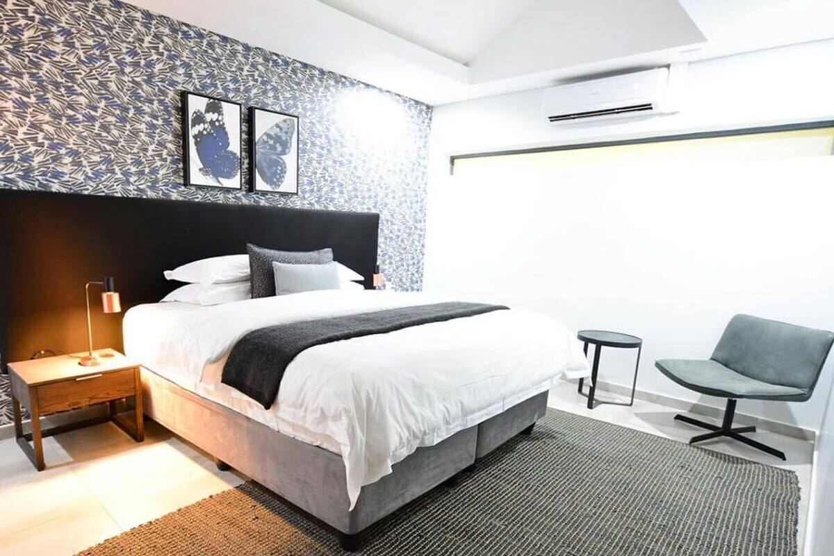 Ein modernes Hotelzimmer mit einem großen Bett, einem Nachttisch, einem Sessel und einer Wand mit Muster.