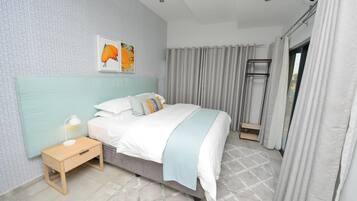 A bedroom with a bed, a nightstand, a window with curtains, and a wall with a geometric pattern.