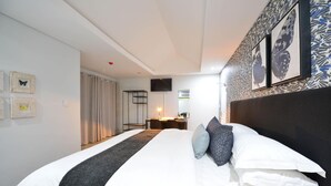 Hotellihuone, jossa on suuri sänky, työpöytä tuolilla, seinälle asennettu taulutelevisio ja ikkuna, jossa on verhot.