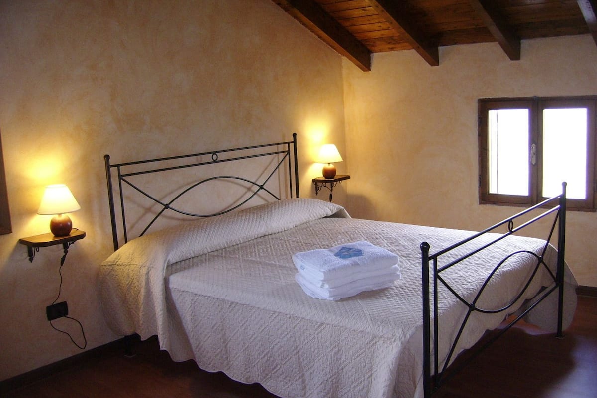 A bedroom with a bed, two bedside lamps, a window, and a wooden ceiling.