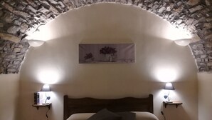 A bedroom with a stone wall, a wooden headboard, two bedside lamps, and a painting above the bed. - Agriturismo Al Pagan (Pigna)