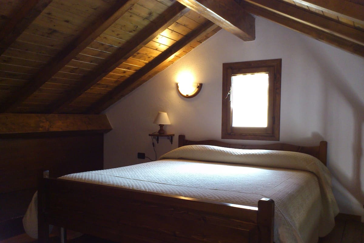 A wooden bed in a room with a sloped ceiling and a window.
