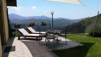 A terrace with a table and chairs, a sunshade, and potted plants.