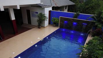 Ein Swimmingpool mit blauer Fliesenbordur, umgeben von Kübelpflanzen und einem Gebäude mit einem geflasten Dach.