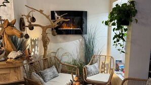 A cozy living room with wicker furniture, a fireplace, and a large window with a plant. - Hotel le Médieval (Aigues-Mortes)