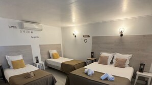 A hotel room with three beds, each with a brown bedspread and white pillows. There are wall-mounted lights, a small table with a lamp, and a wall-mounted air conditioner. - Hotel le Médieval (Aigues-Mortes)