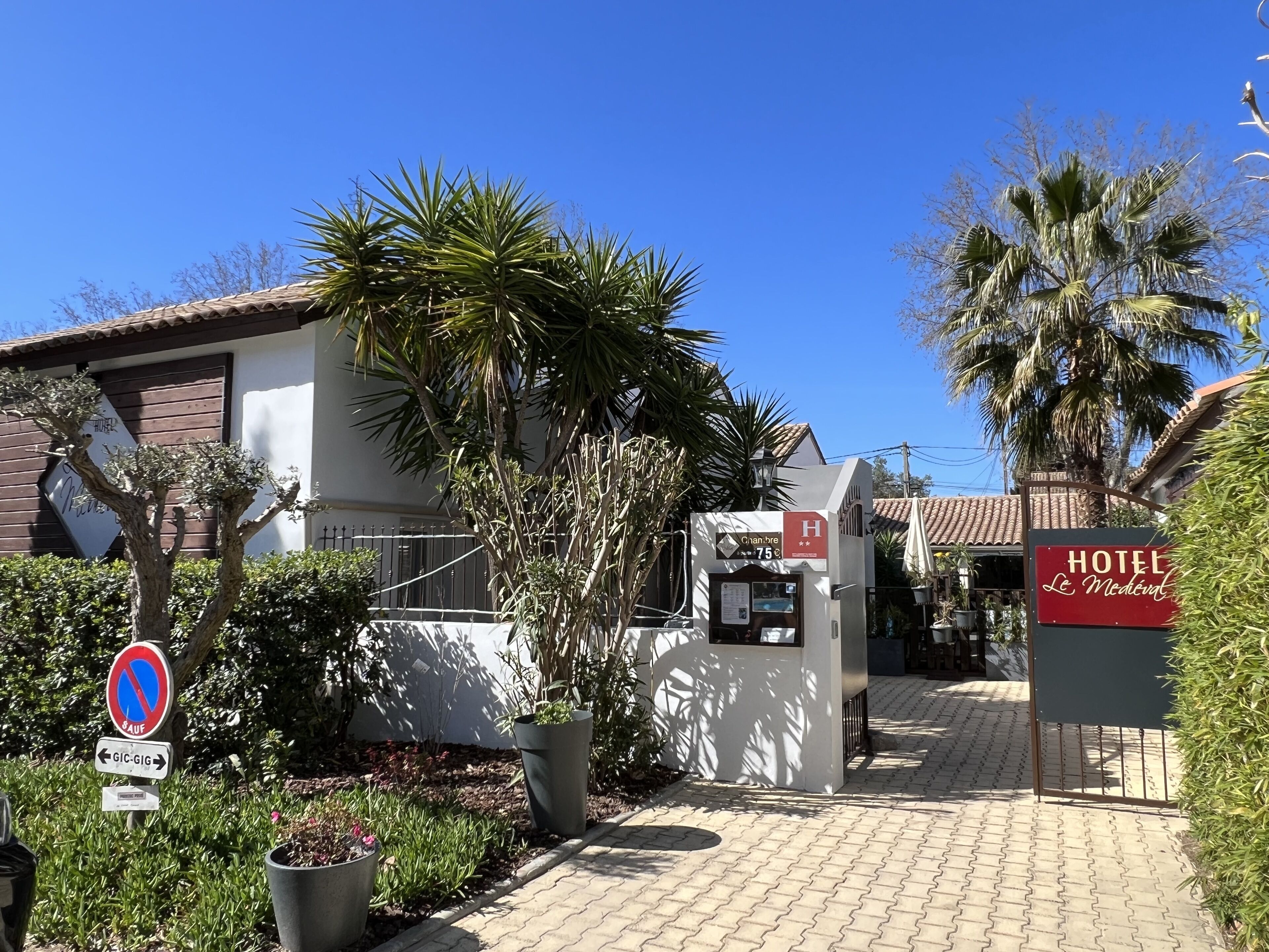 Entrada de hotel com um letreiro indicando o preço de 75 euros, uma placa de proibido estacionar e uma placa de direção para 'GIC-GIG'.
