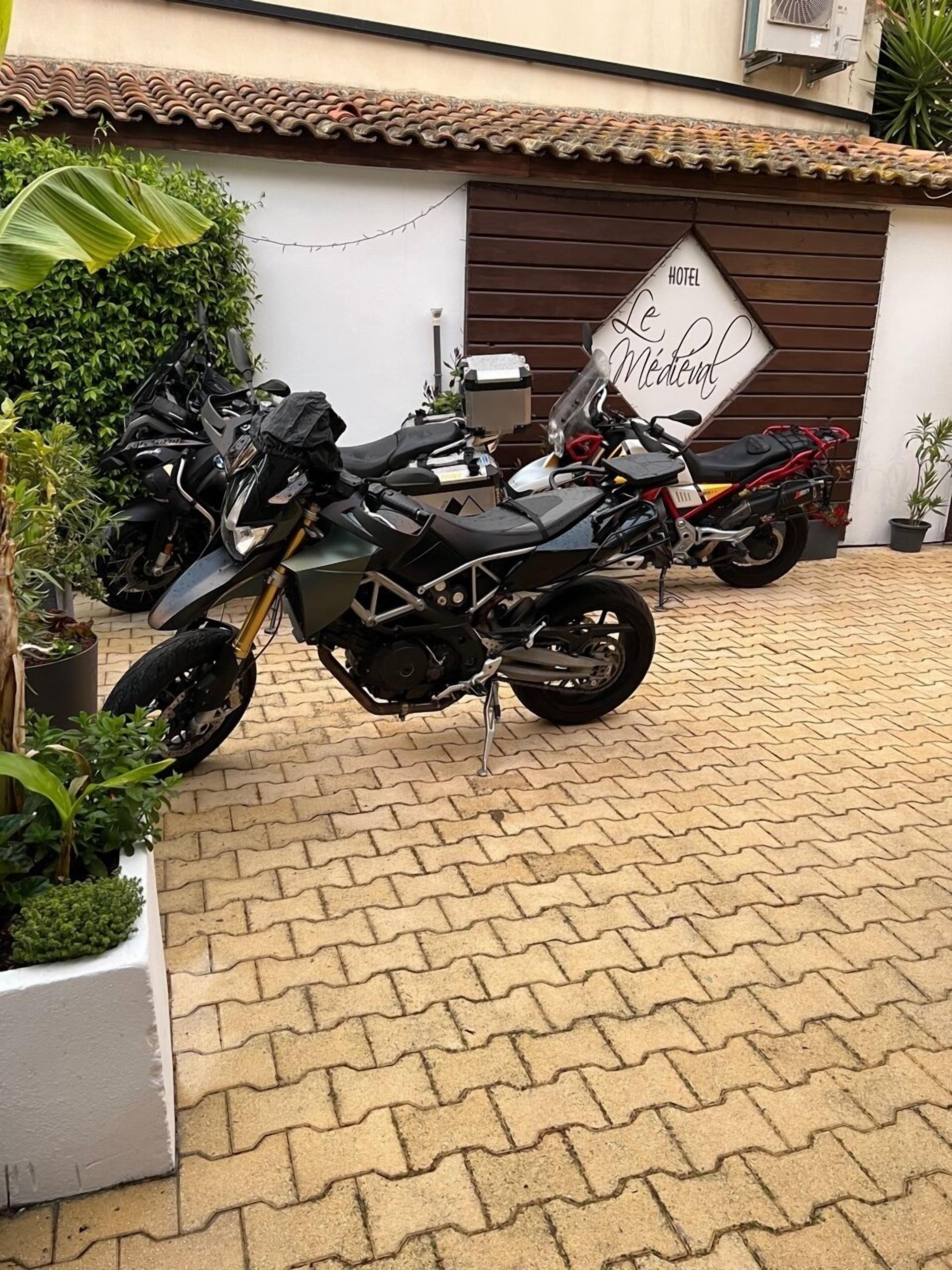 Une moto est garée devant un immeuble sur lequel on peut lire l’inscription « HÔTEL Médem ».