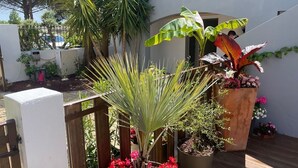 A wooden deck with potted plants and flowers, a white wall, and a metal gate. - Hotel le Médieval (Aigues-Mortes)