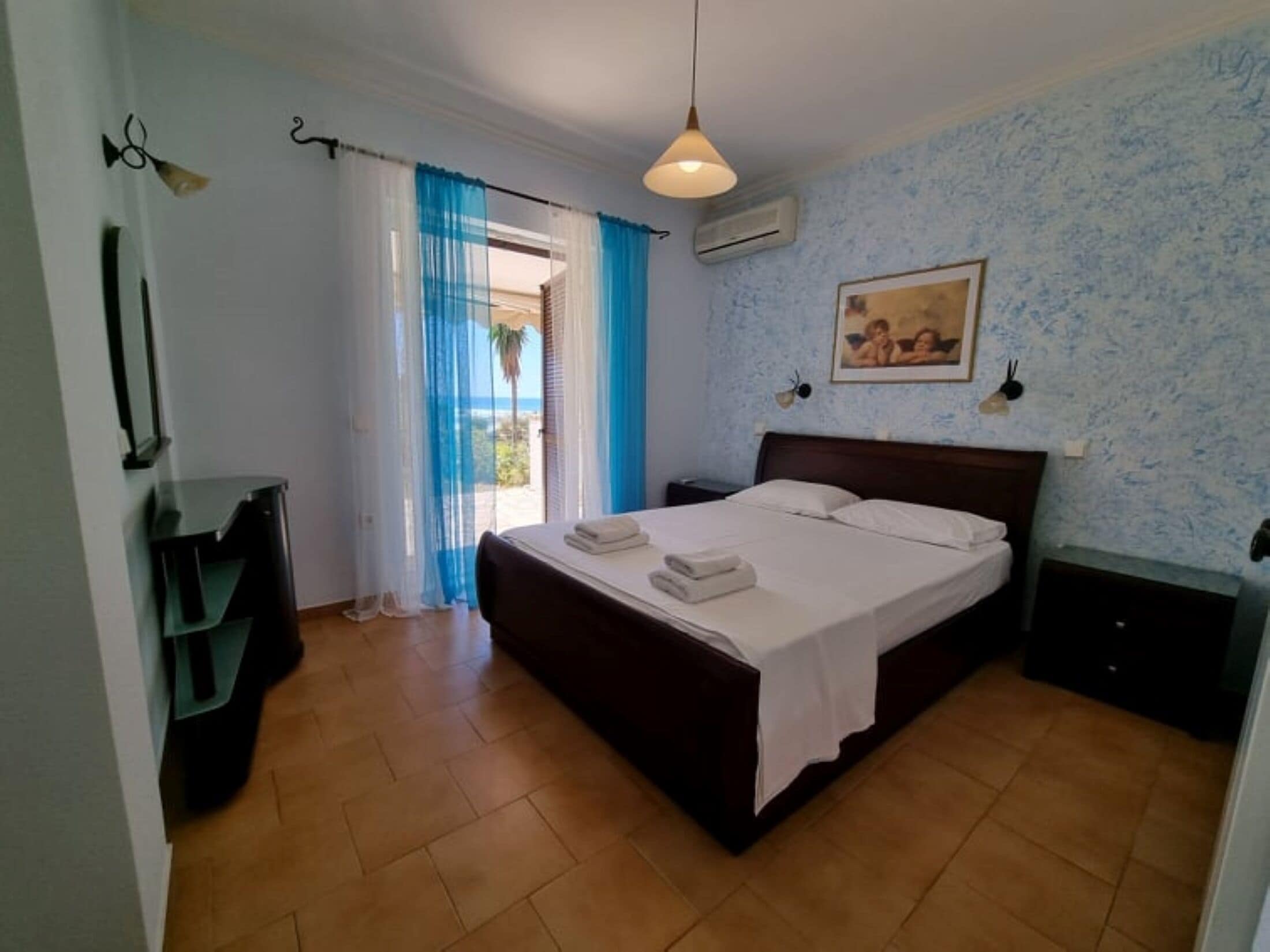 Une chambre à coucher comprenant un lit, une table de chevet, un bureau, une chaise, une fenêtre avec des rideaux et un tableau accroché au mur.