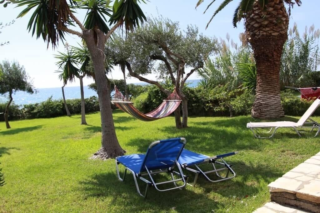 Area verde all'aperto con un'amaca, due poltrone da relax e una palma.