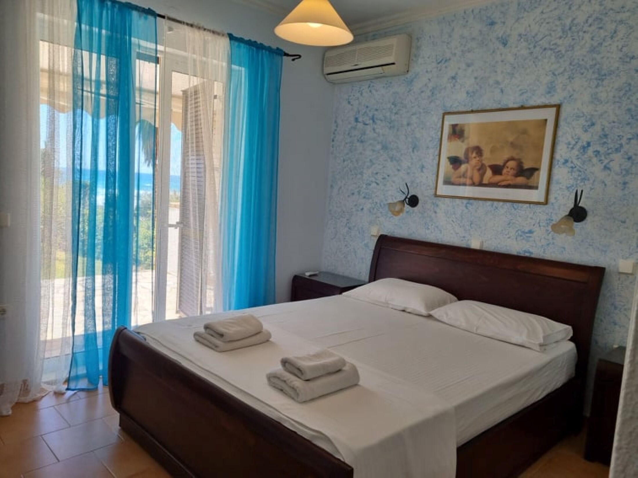 Quarto com cama, mesa de cabeceira, ar condicionado fixado na parede e janela com cortinas azuis.