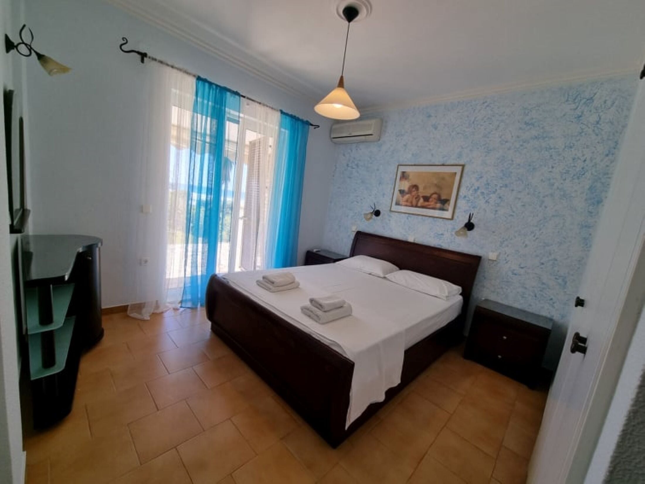 Un dormitorio con cama, escritorio, silla, un cuadro en la pared y ventana con cortinas.