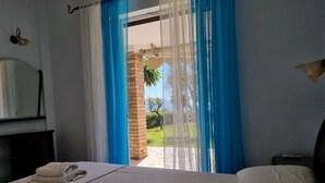 A hotel room with a bed, a desk, and a view of the outdoors through a window with blue curtains. - Corfu Island Apartment 58 (Corfu)