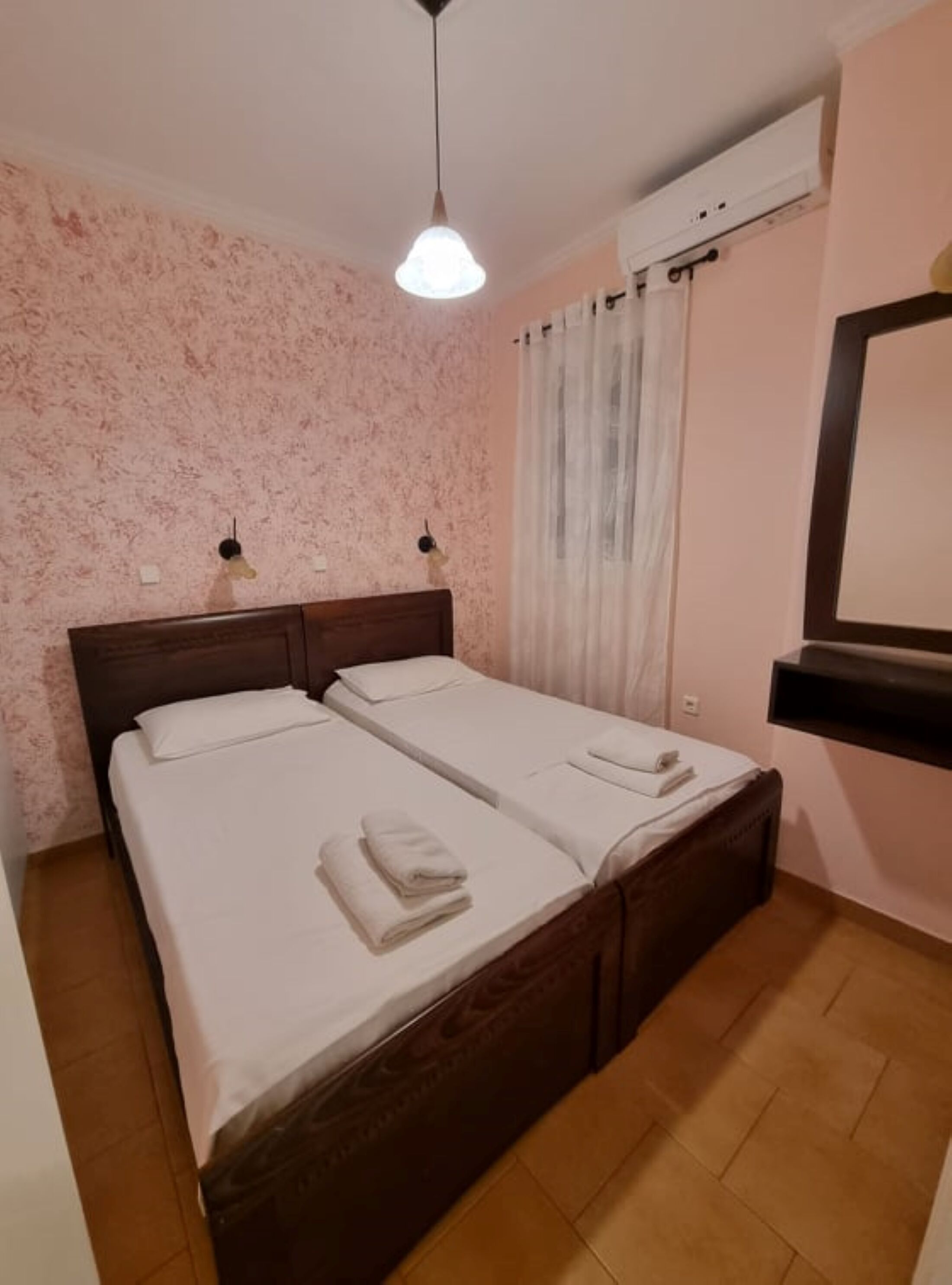 Habitación doble con dos camas, cabecero de madera, luz de techo, aire acondicionado y un espejo en la pared.