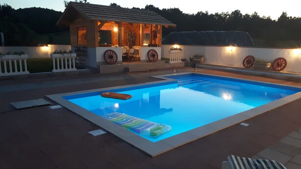 Ein Schwimmbecken mit Sonnendeck, ein kleines Gebäude mit Veranda und dekorative Räder.