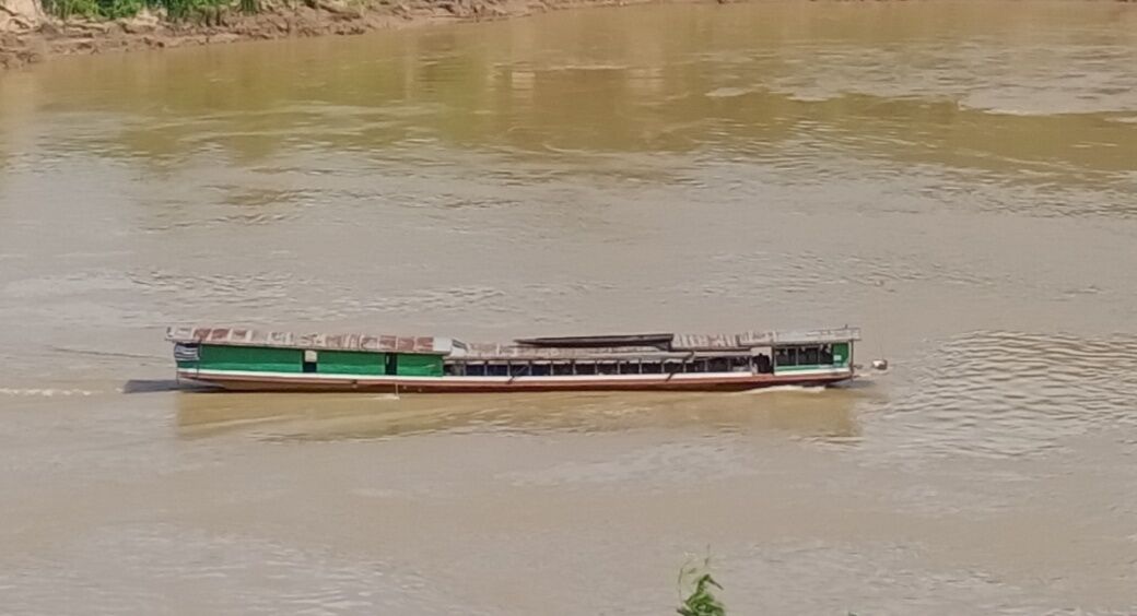 Una embarcación larga y delgada con una decoración verde y blanca, navegando en un río.