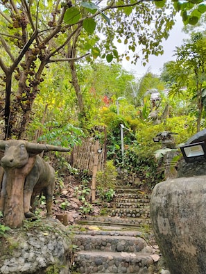 A garden pathway with a stone staircase, surrounded by lush greenery and a decorative bull statue. - Art Khamu Homestay (Chiang Khong)
