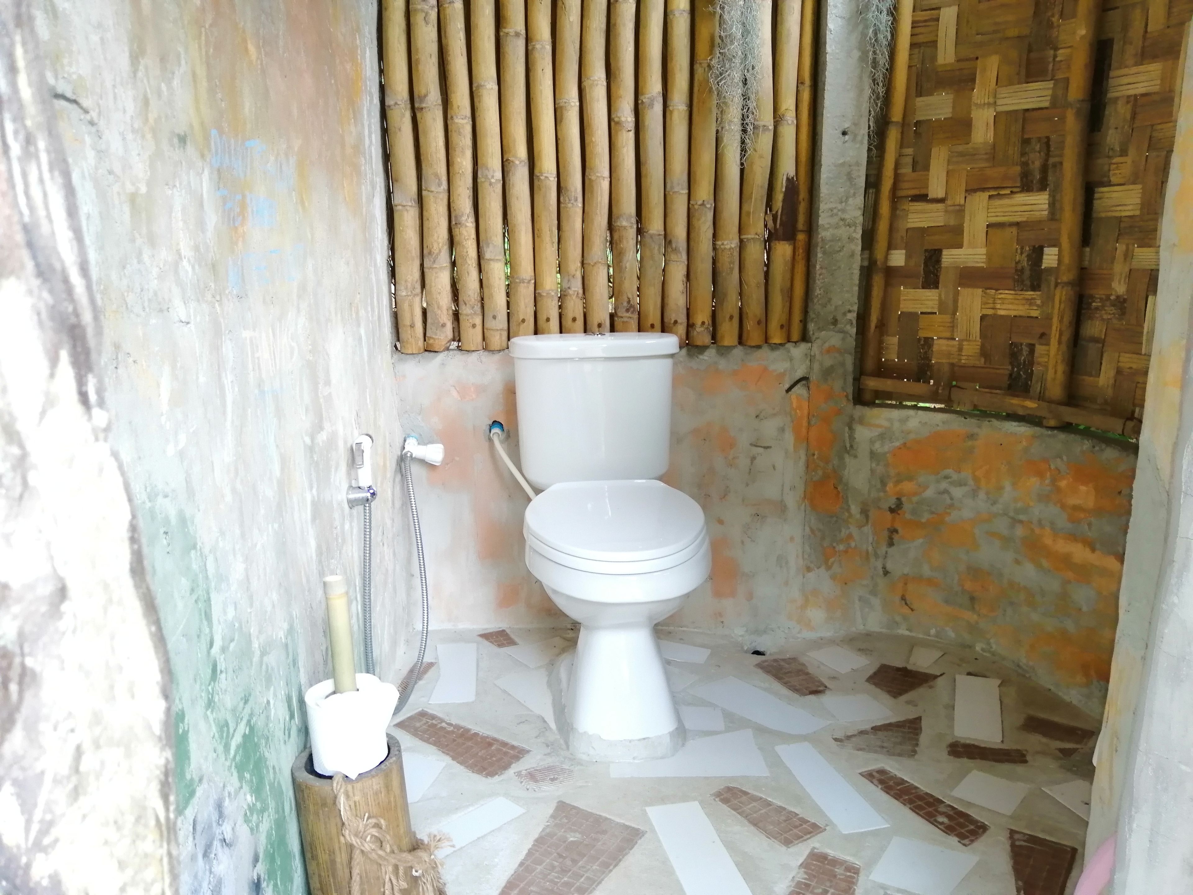 Une salle de bain avec des toilettes, un mur en bambou et un sol carrelé.