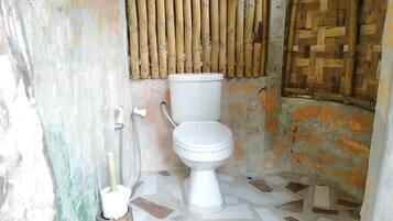 Un baño con inodoro, pared de bambú y suelo de baldosas.