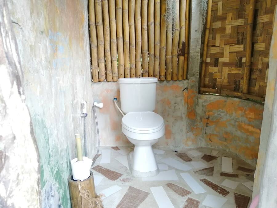Un baño con inodoro, pared de bambú y suelo de baldosas.