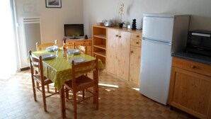 A compact kitchen with wooden cabinets, a dining table with chairs, a refrigerator, and a microwave.