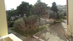 A view from a balcony overlooking a courtyard with trees and a building in the background.