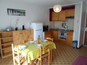 Une cuisine compacte avec des meubles en bois, une table à manger pour quatre personnes, un réfrigérateur, un four à micro-ondes et un luminaire suspendu.