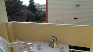A small balcony with a table and two chairs, a kettle, and a cup.